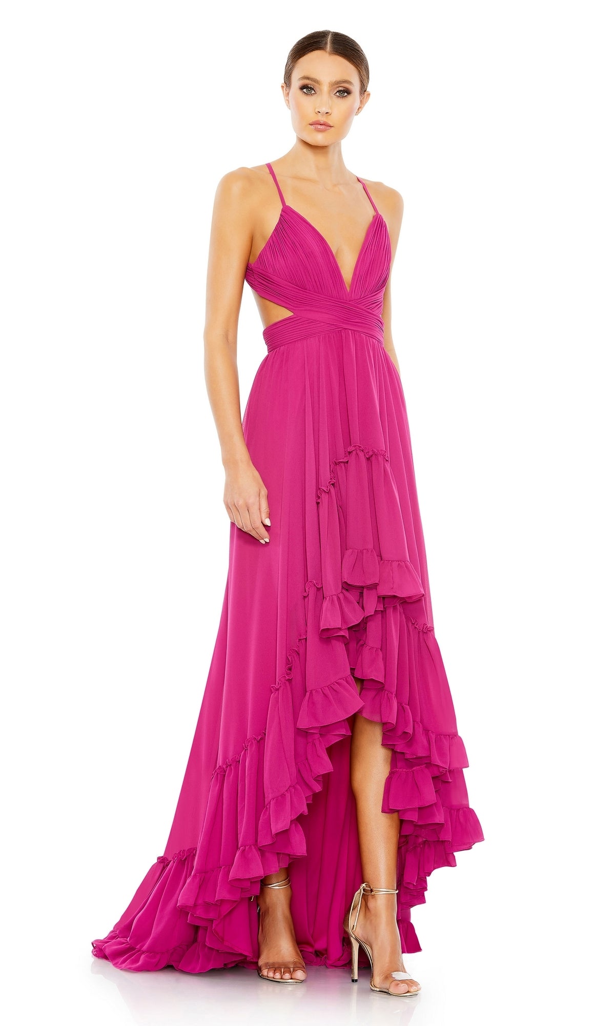 A woman wears the Mac Duggal 67992 Fuchsia High-Low Formal Dress with ruffle details, deep V-neck, cutout sides, and a dramatic hemline, perfectly styled with metallic high-heeled sandals.